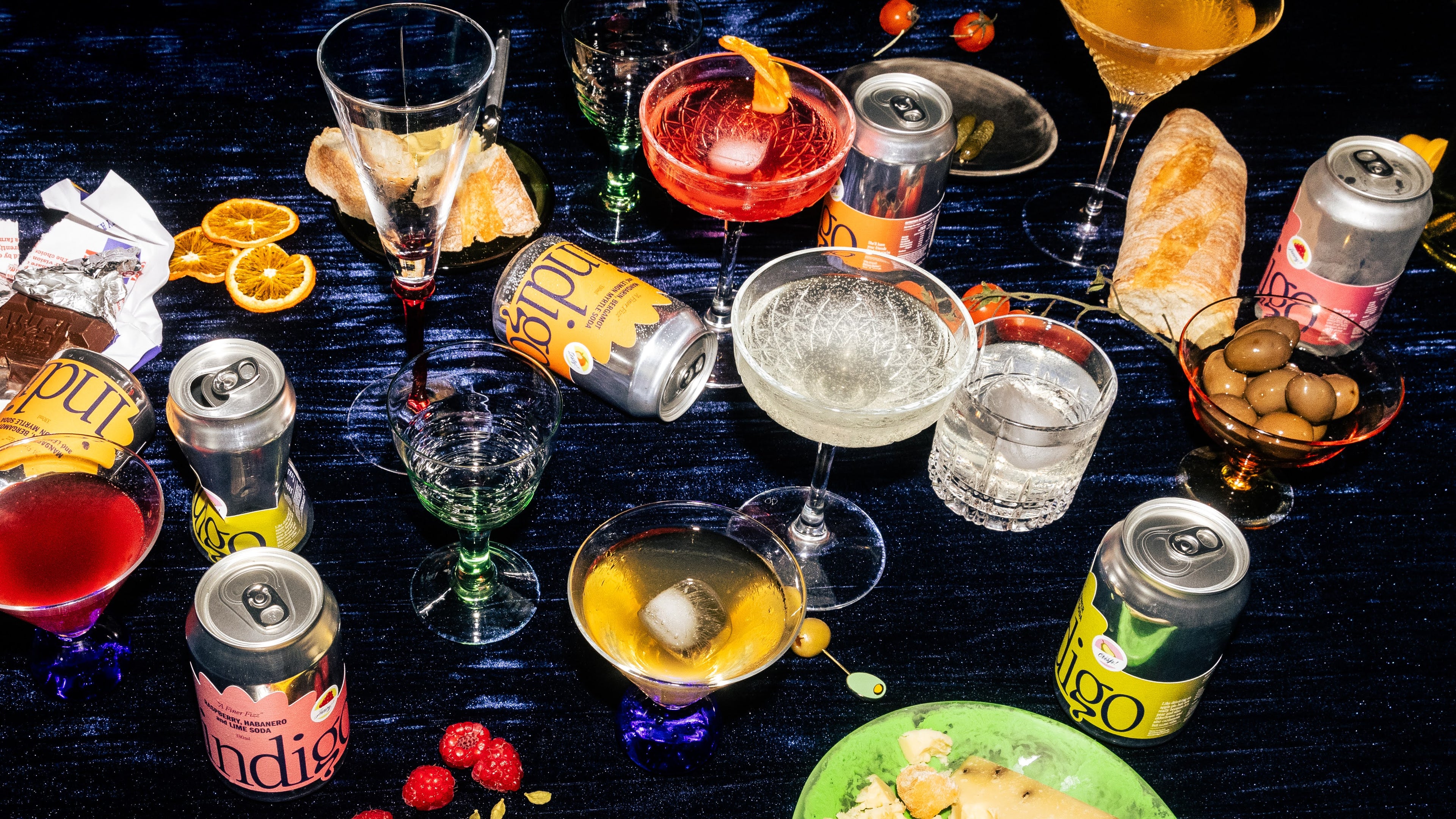 Indigo botanical soda cans in three flavours – mandarin bergamot and lemon myrtle, raspberry habanero and lime, and pear elderflower and cardamom – arranged in a tablescape.