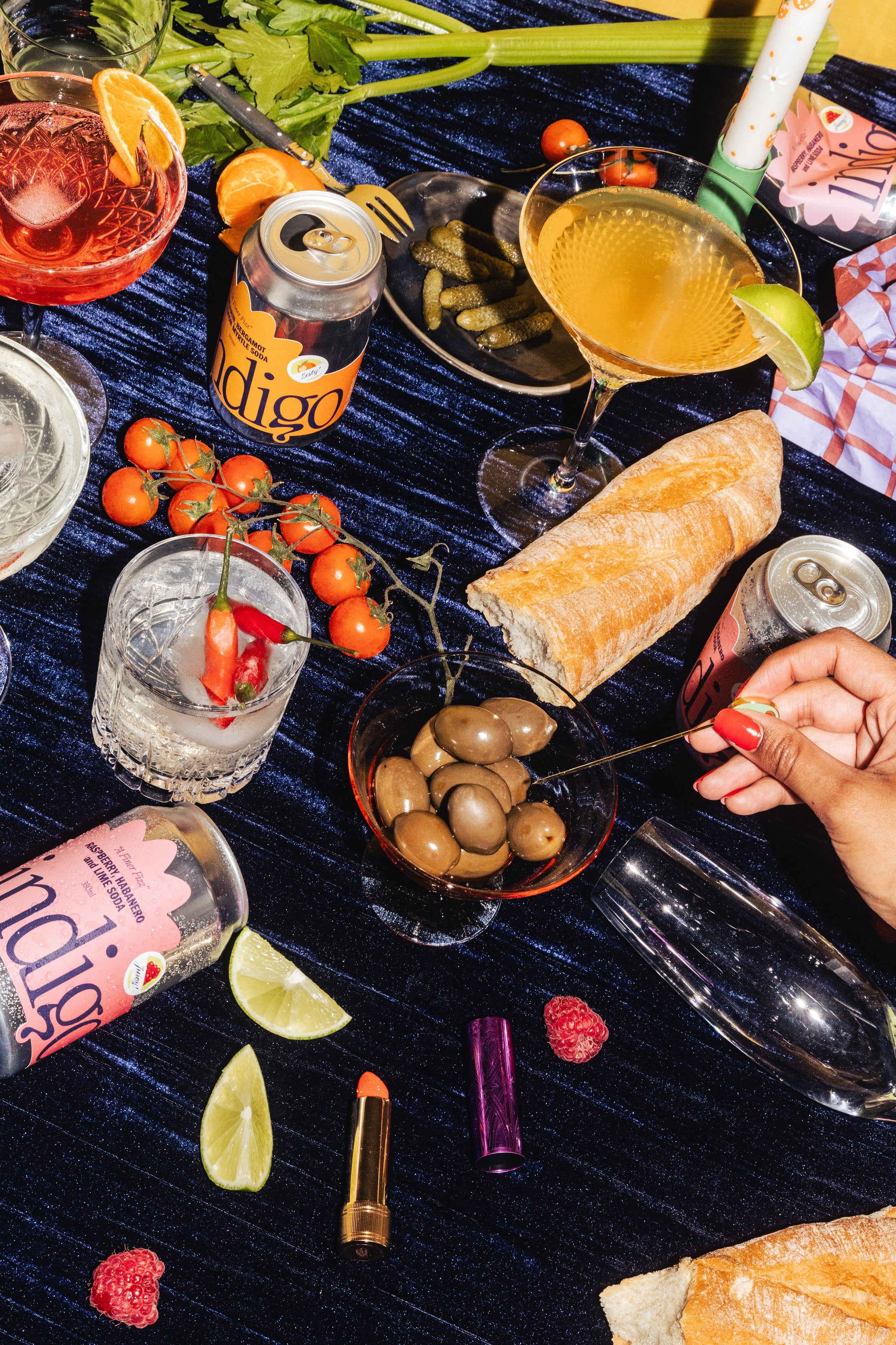 A messy tablescape on a velvet tablecloth, there are various cans of indigo strewn on the table, Raspberry indigo, Mandarin indio and Pear indigo