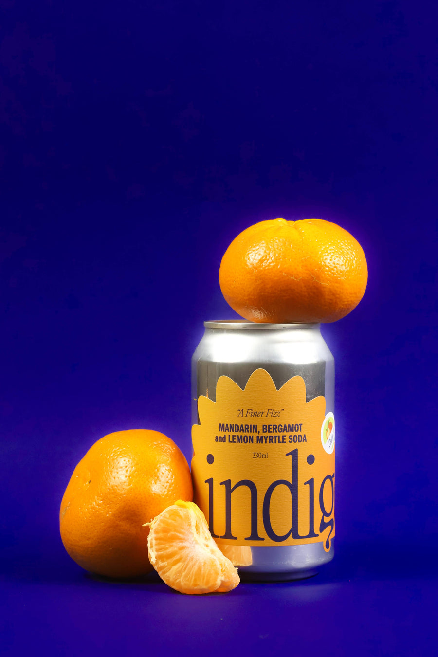 A can of Indigo mandarin, bergamot, and lemon myrtle soda with a blue background and a slice of mandarin orange in the foreground.