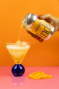 Load image into Gallery viewer, A can of indigo Mandarin, Bergamot and Lemon Myrtle soda being poured into a glass, there is mandarin in the foreground and fizzy bubbles in the glass.
