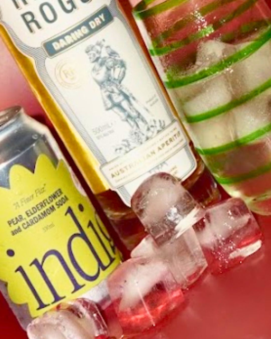 The two ingredients in The blanc space – a can of indigo Pear, Elderflower & Cardamom soda and a bottle of Regal Rogue Daring Dry vermouth, beside the finished drink in a green-striped tumbler and loose ice cubes